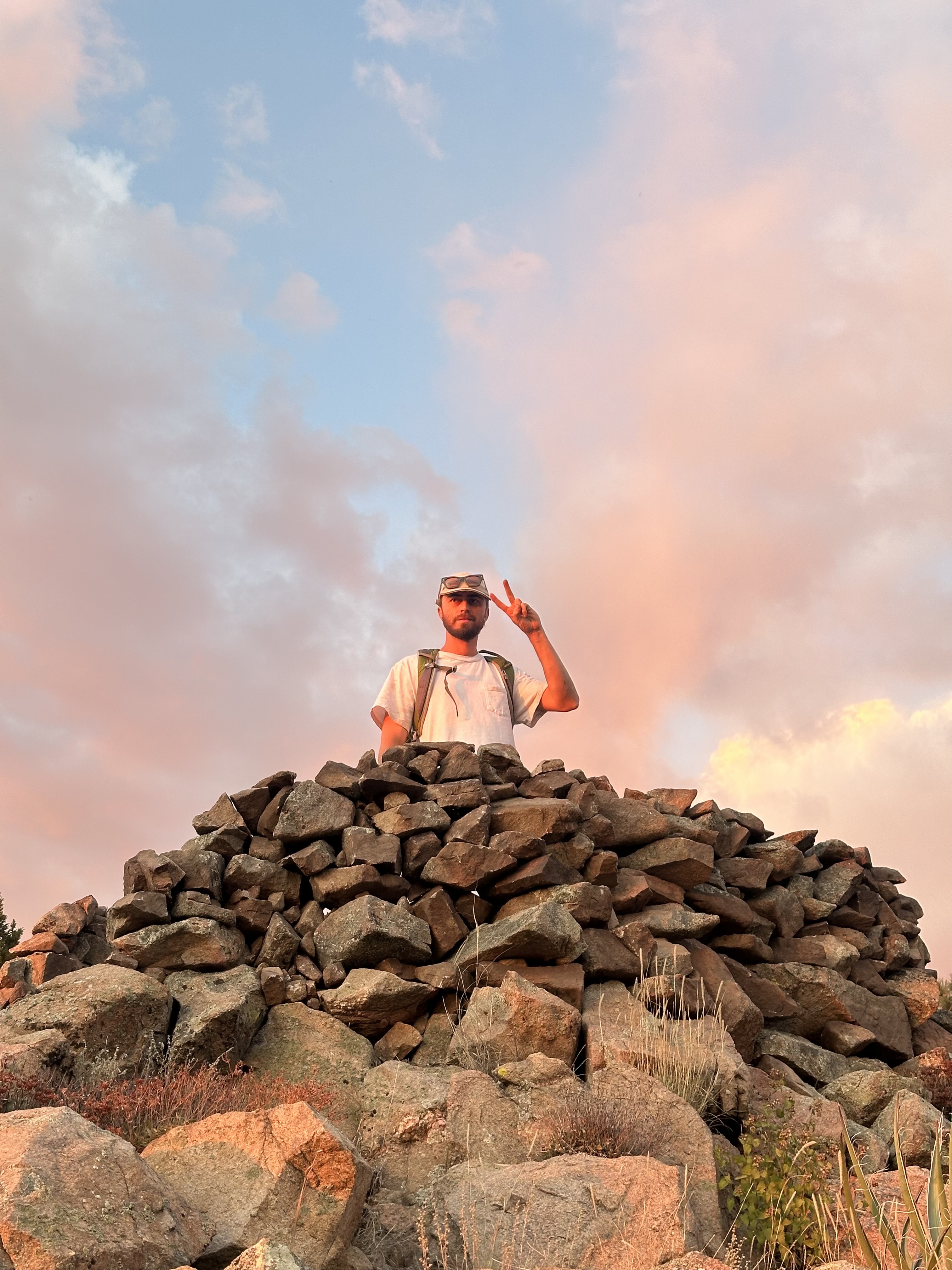 Builder behind stone cairn — peace sign, pink clouds